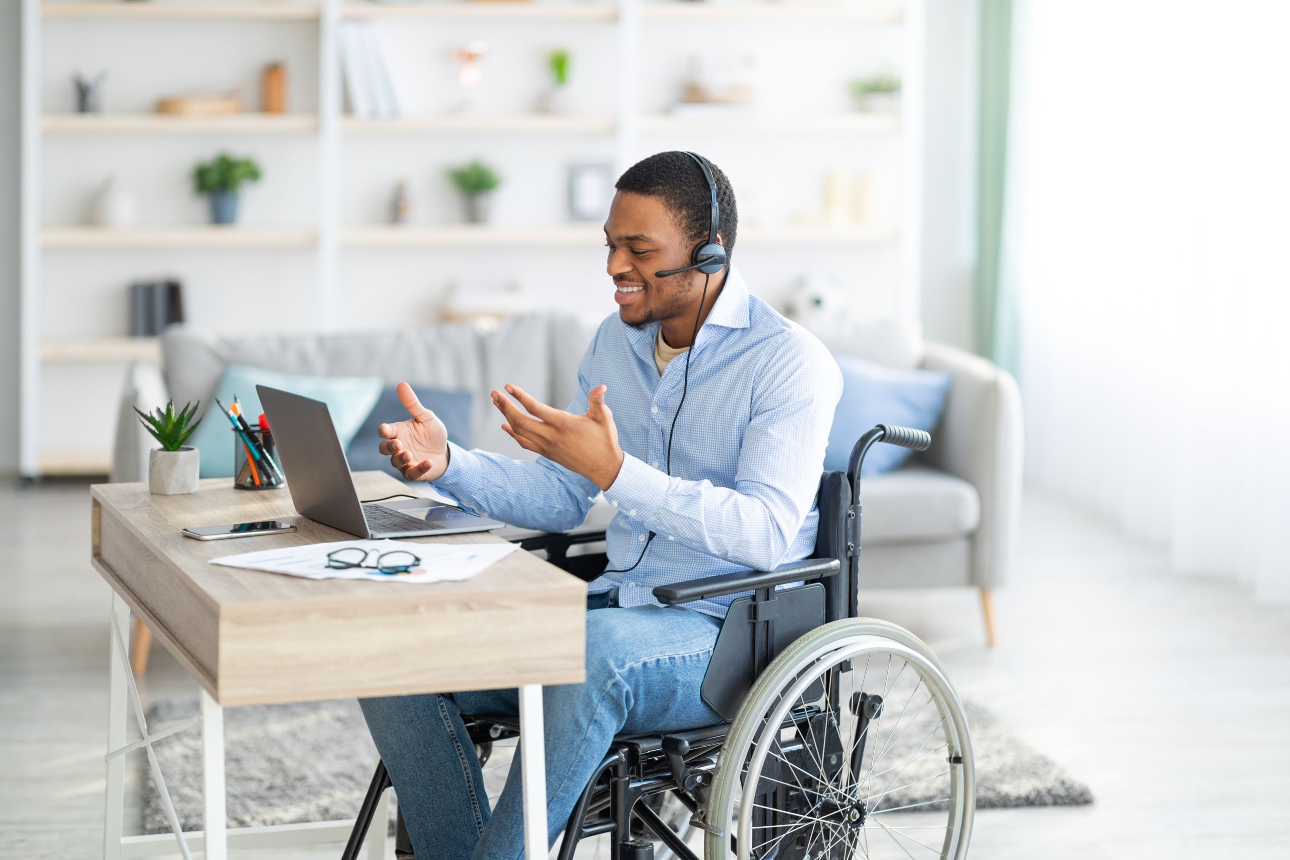 Disabled guy with headset communicating online on laptop, having business meeting from home